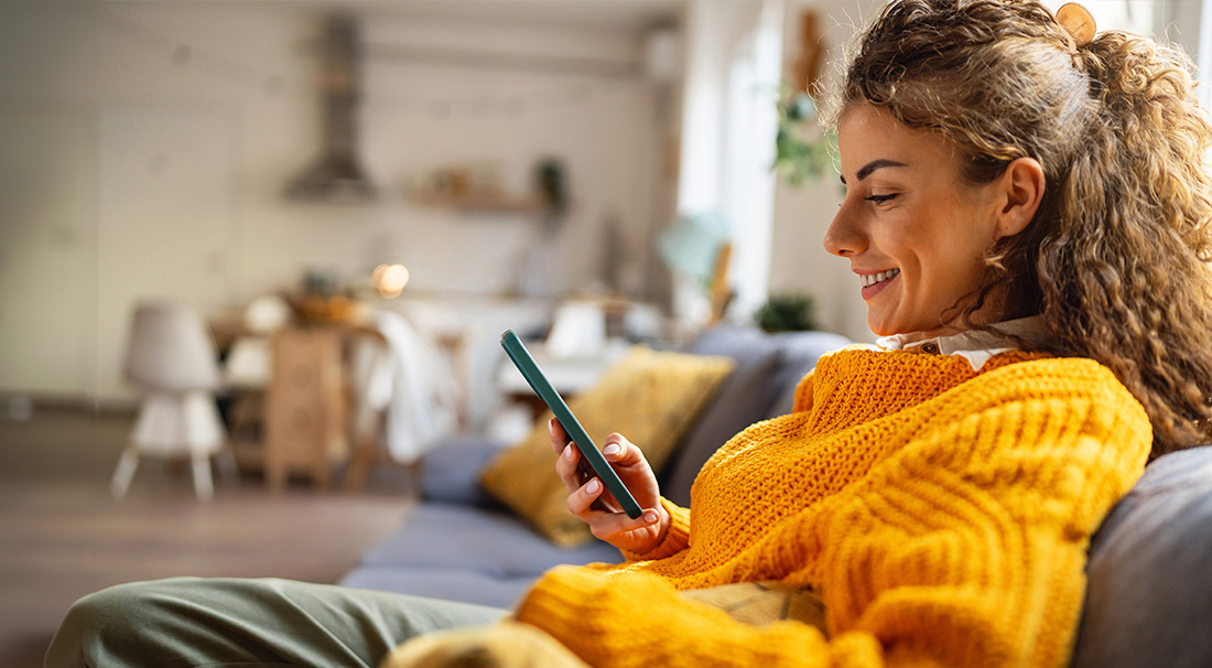 Vrouw zit op de bank en kijkt op haar mobiel