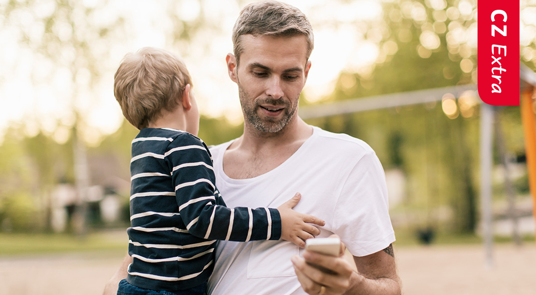 Man houdt een kind vast en kijkt op zijn mobiel